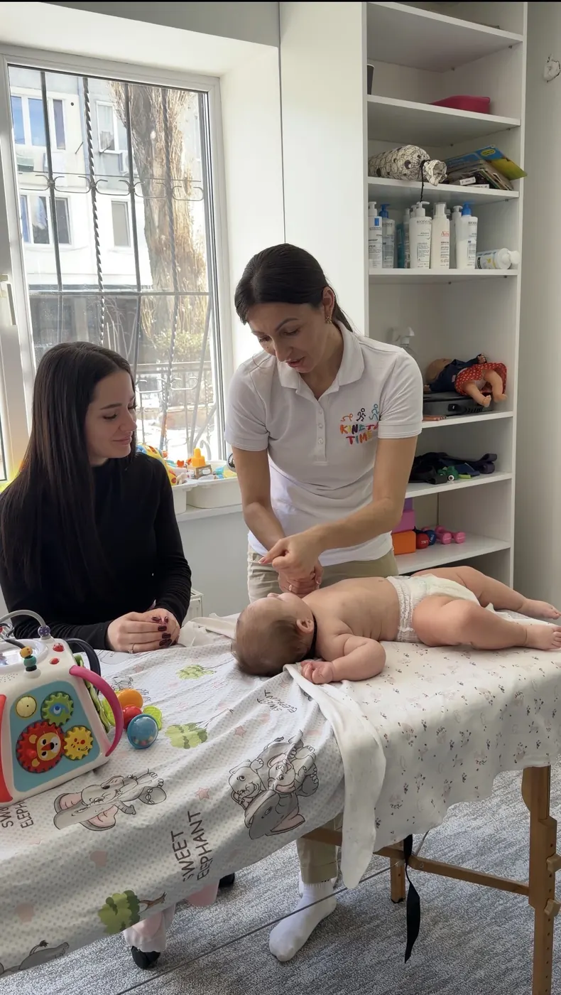 Două specialiste KINETO TIME la masa de masaj, cu un bebeluș întins pe burtă